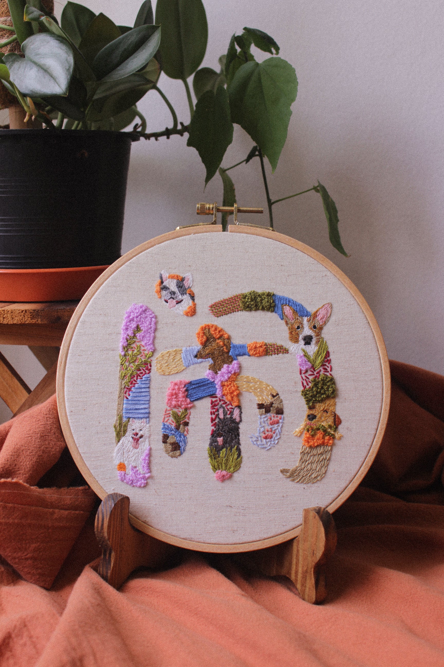 Embroidery hoop with a colorful design of dogs and text on a wooden stand.